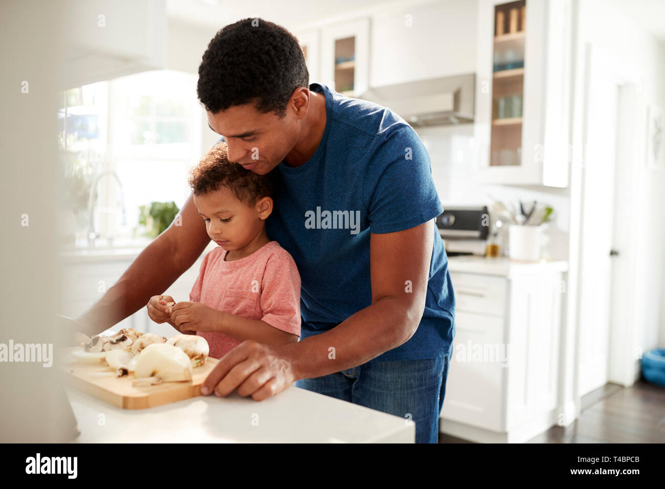 Millennial man standing at kitchen worktop preparing food with his toddler son, close up, selective focus Stock Photo