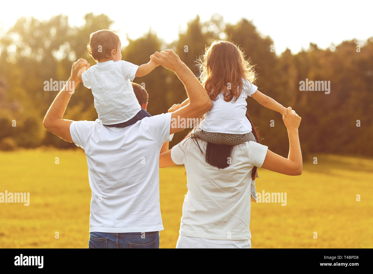 View from behind. A family with children are walking on the grass in a park . Stock Photo