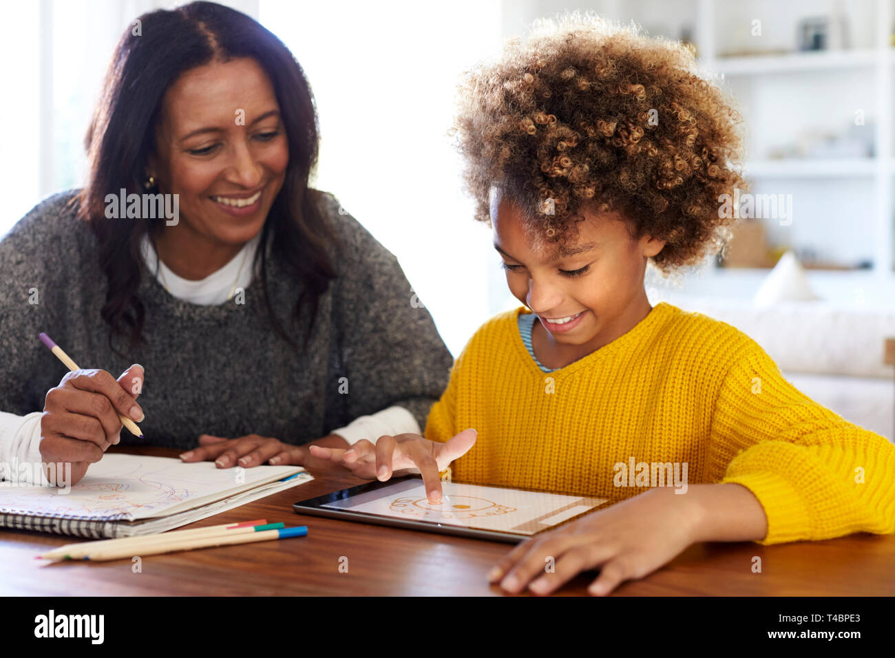 Mixed race young grandmother sitting at table doing homework with her granddaughter using a tablet computer, close up Stock Photo