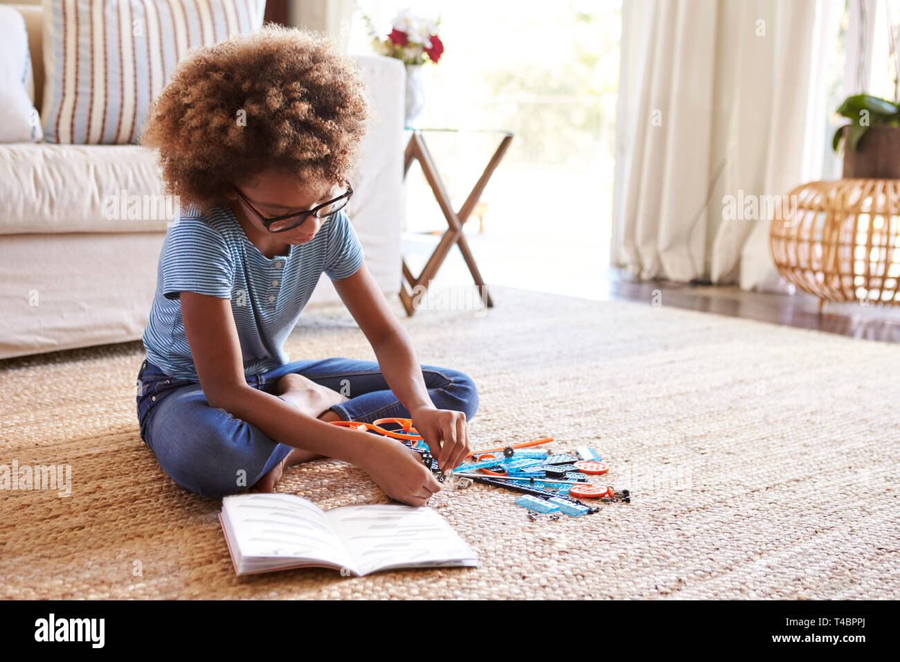 Pre-teen girl sitting on the floor in the living room reading instructions and constructing a model, close up Stock Photo