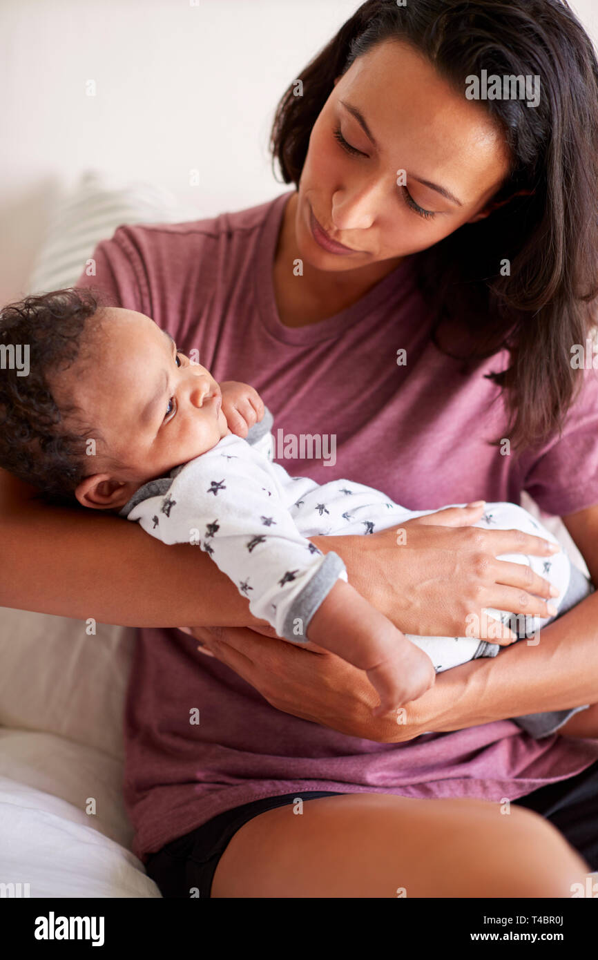 Millennial mixed race mother  sitting on her bed holding her three month old baby son in her arms, vertical Stock Photo