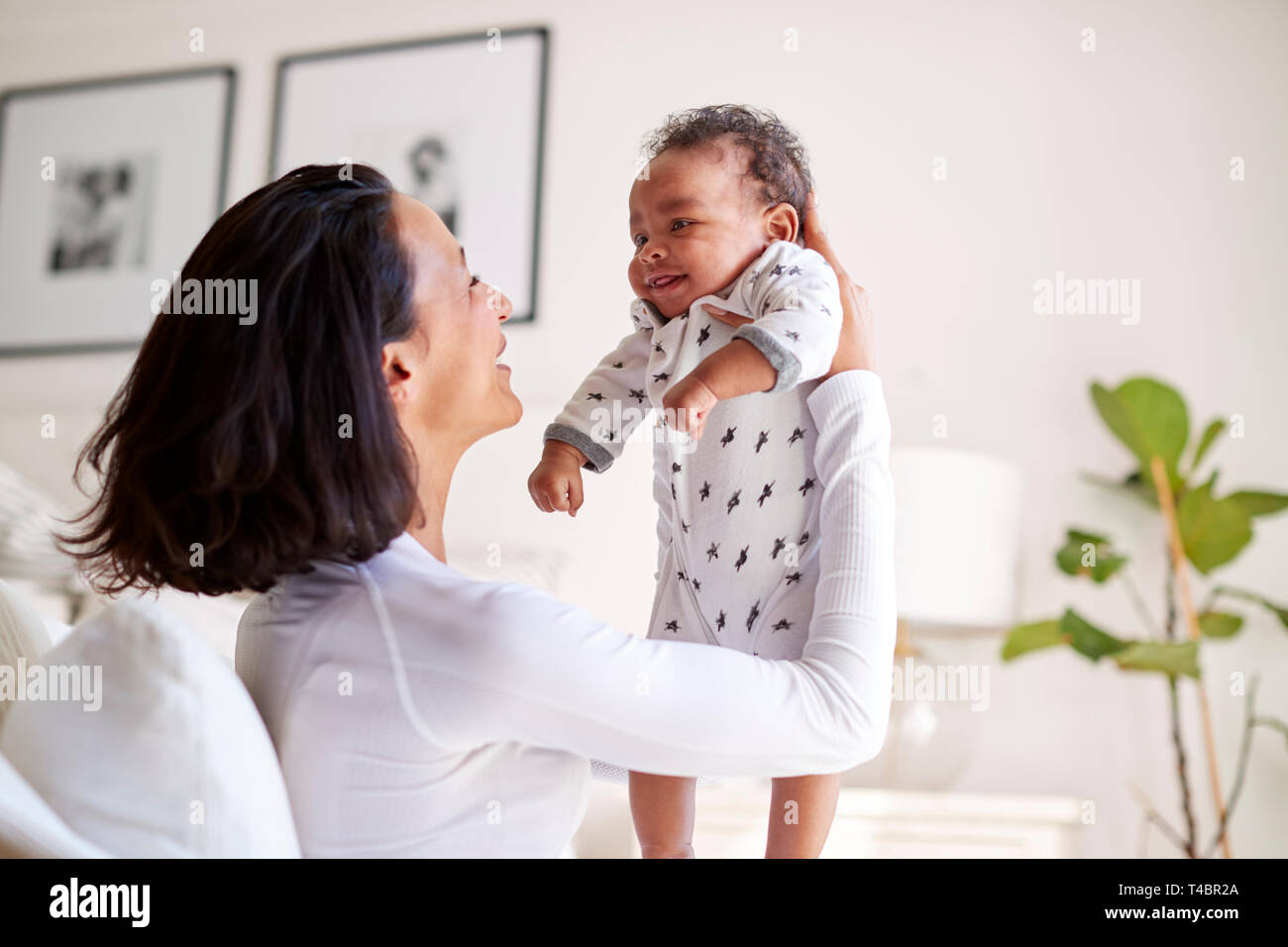 Happy mixed race young adult mother raising her three month old baby son in the air, smiling at him, close up Stock Photo