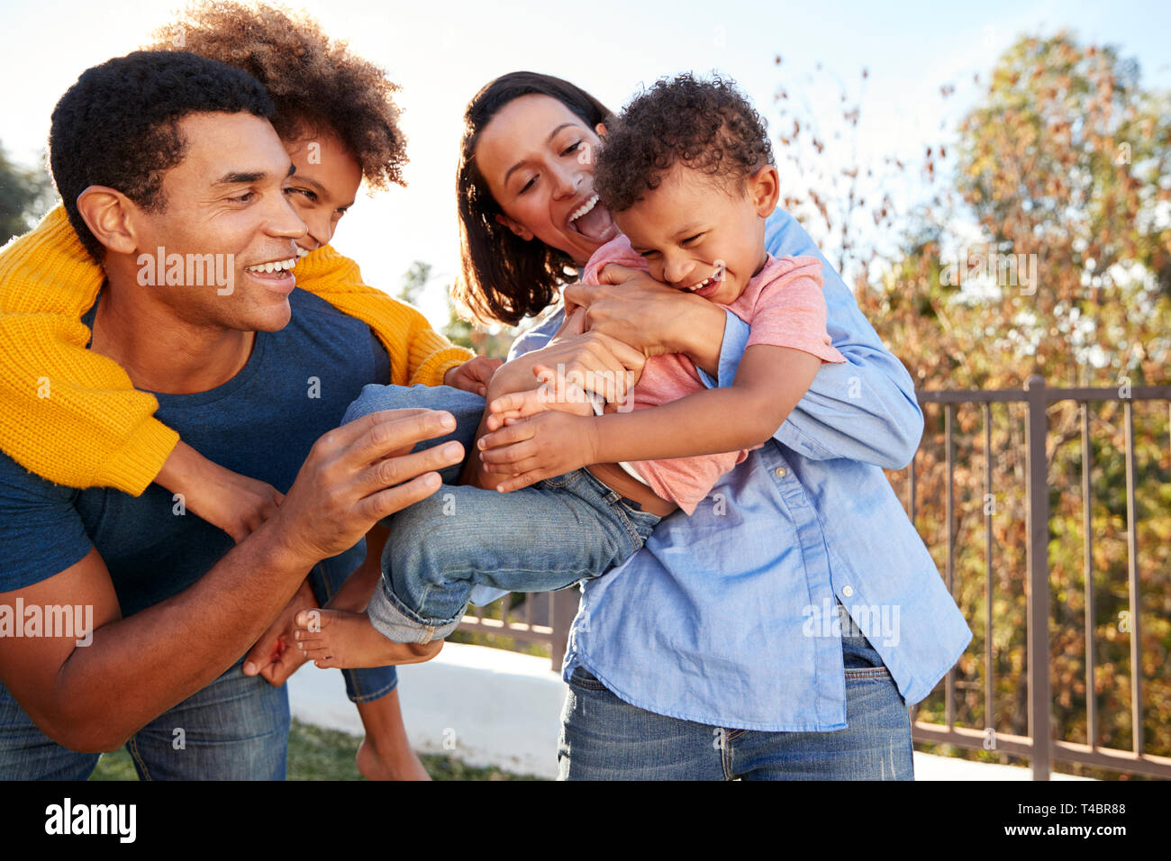 Young mixed race parents playing outdoors carrying their children in the garden Stock Photo