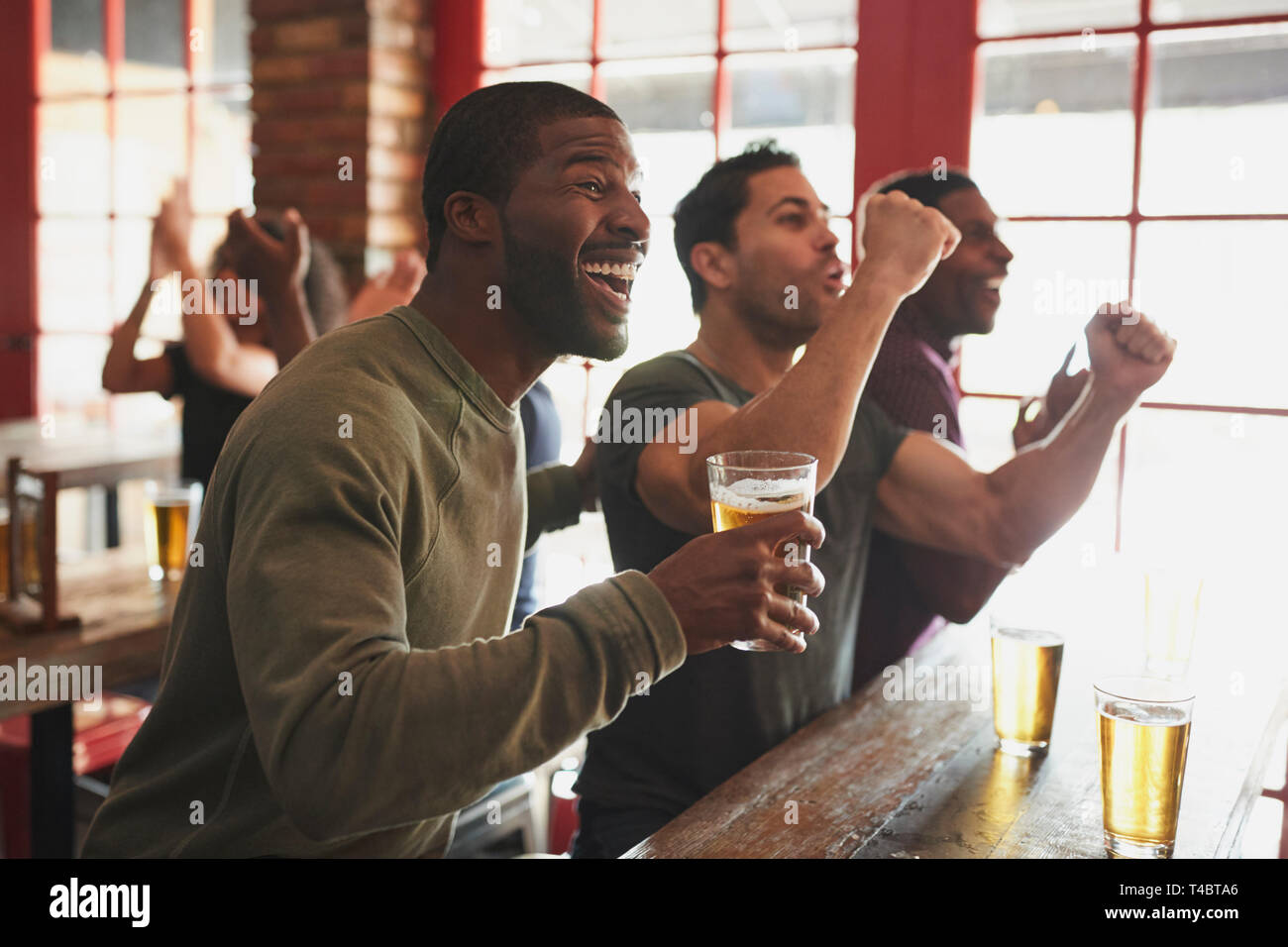 Group Of Male Friends Celebrating Whilst Watching Game On Screen In Sports Bar Stock Photo