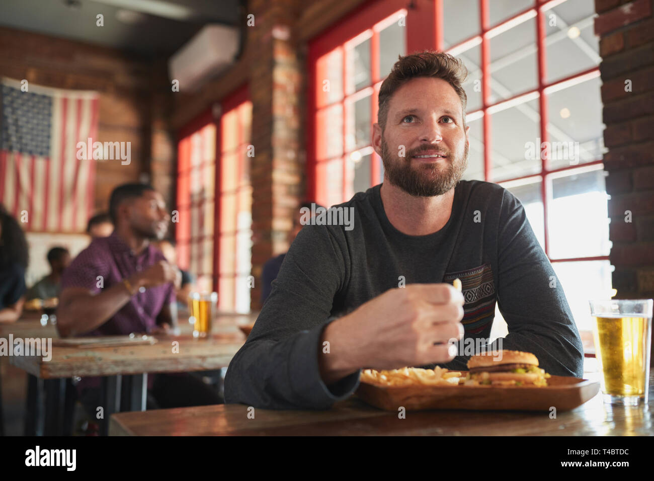 Man Watching Game On Screen In Sports Bar Eating Burger And Fries Stock Photo