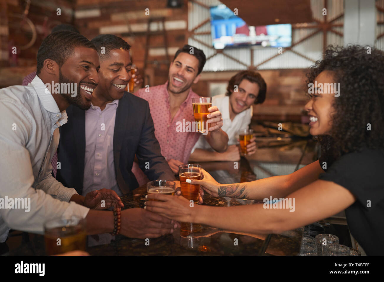 Barmaid Serving Group Of Male Friends On Night Out For Bachelor Party Making Toast Together Stock Photo