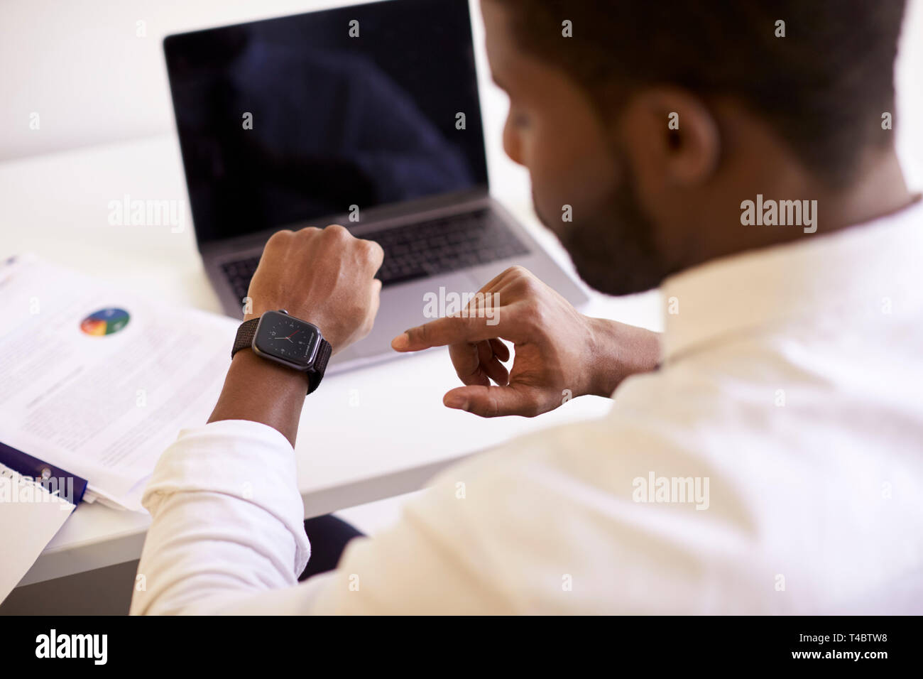 Businessman Working On Laptop At Desk In Modern Office Checking Data On Smart Watch Stock Photo