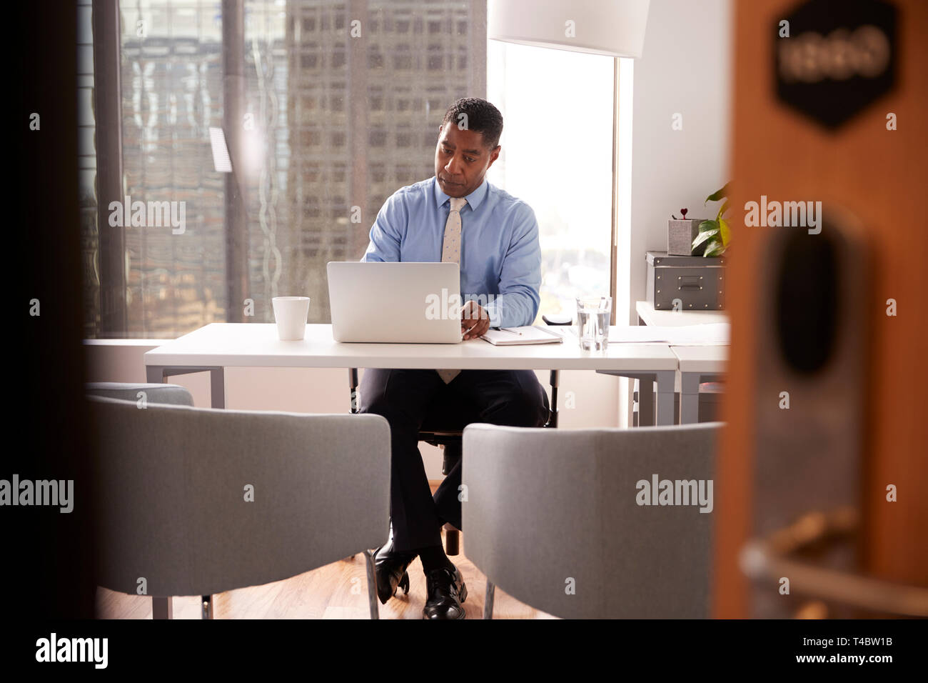 Male Financial Advisor In Modern Office Sitting At Desk Working On Laptop Stock Photo