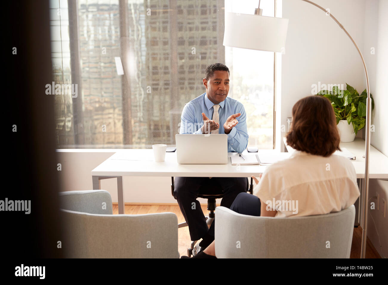 Male Financial Advisor In Modern Office Sitting At Desk Meeting Female Client Stock Photo