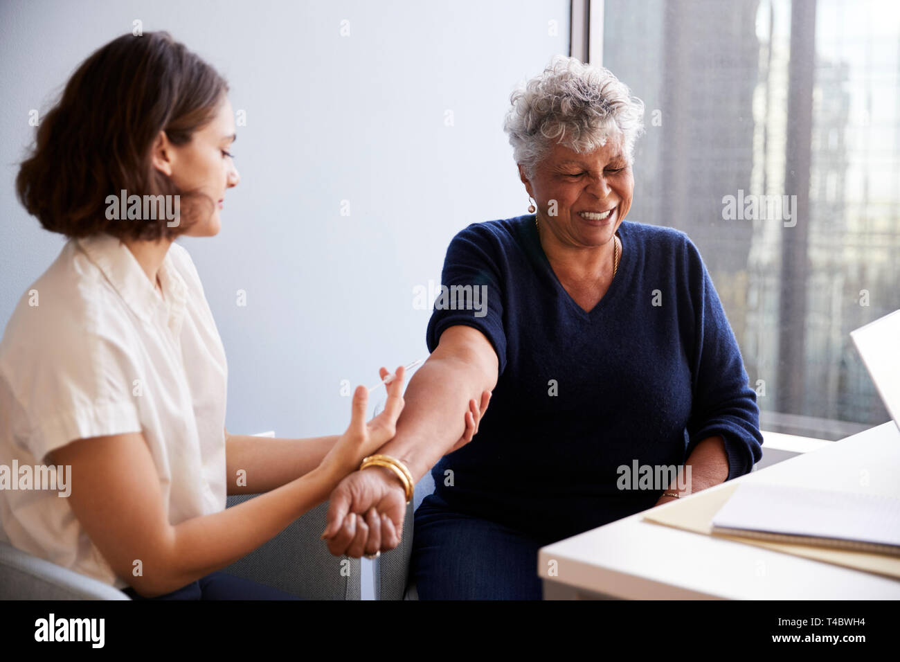 Senior Woman Being Vaccinated With Flu Jab By Female Doctor In Hospital Office Stock Photo