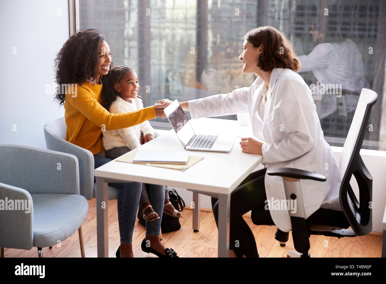 Female Pediatrician Shaking Hands With Mother And Daughter Meeting In Hospital Office Stock Photo