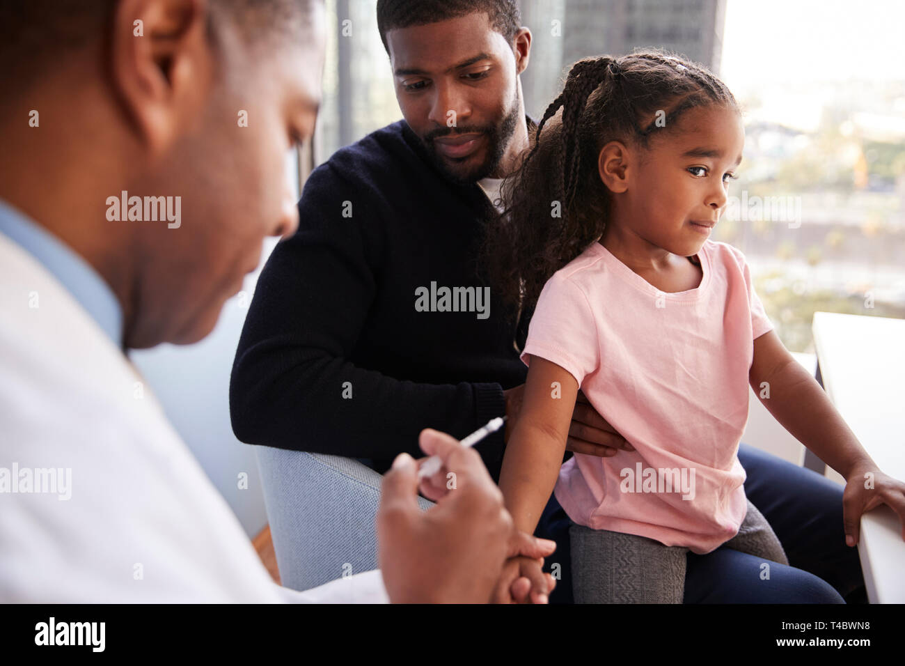 Father Taking Young Daughter For Vaccination In Doctors Office Stock Photo
