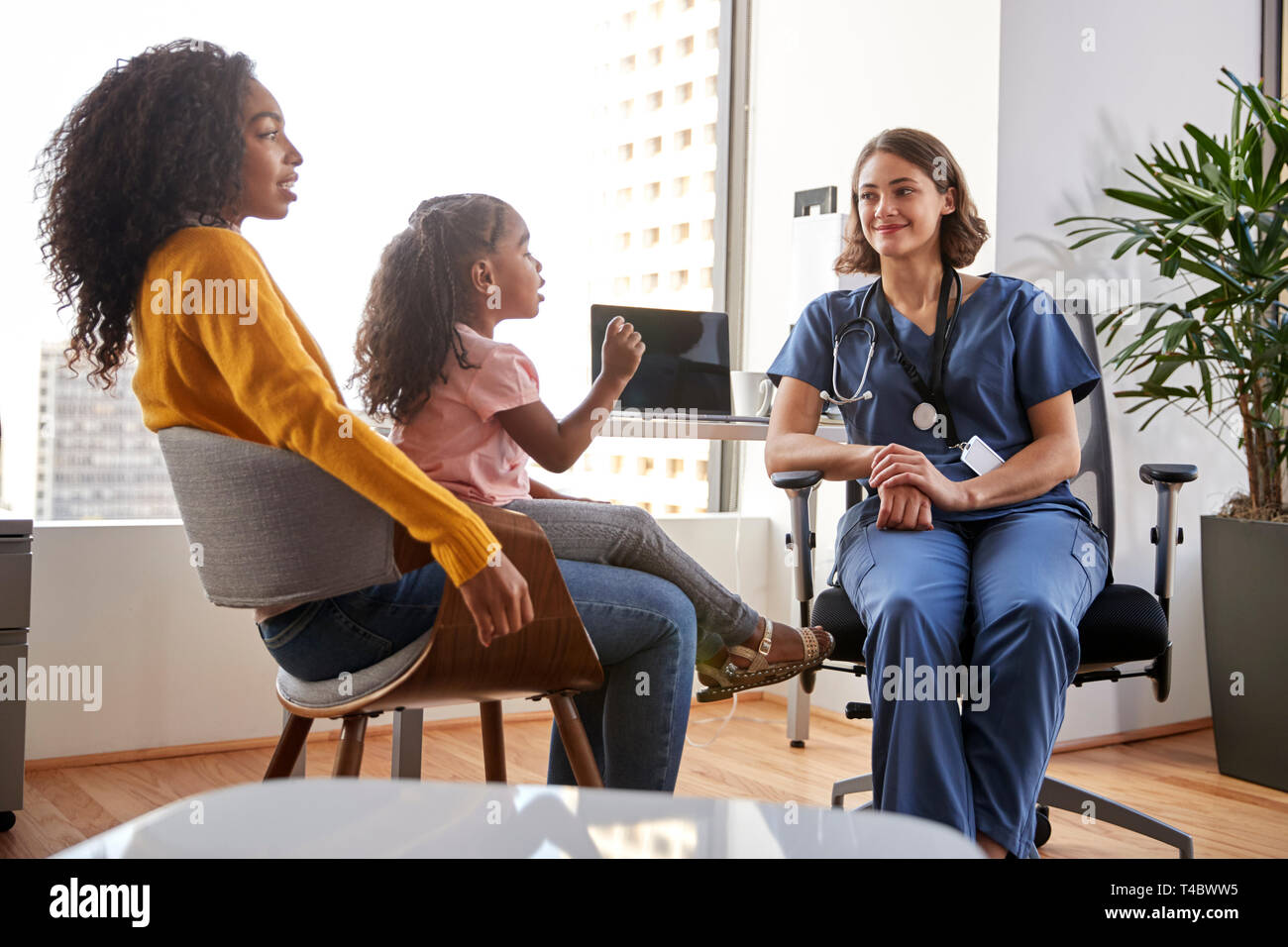 Mother And Daughter Having Consultation With Female Pediatrician Wearing Scrubs In Hospital Office Stock Photo