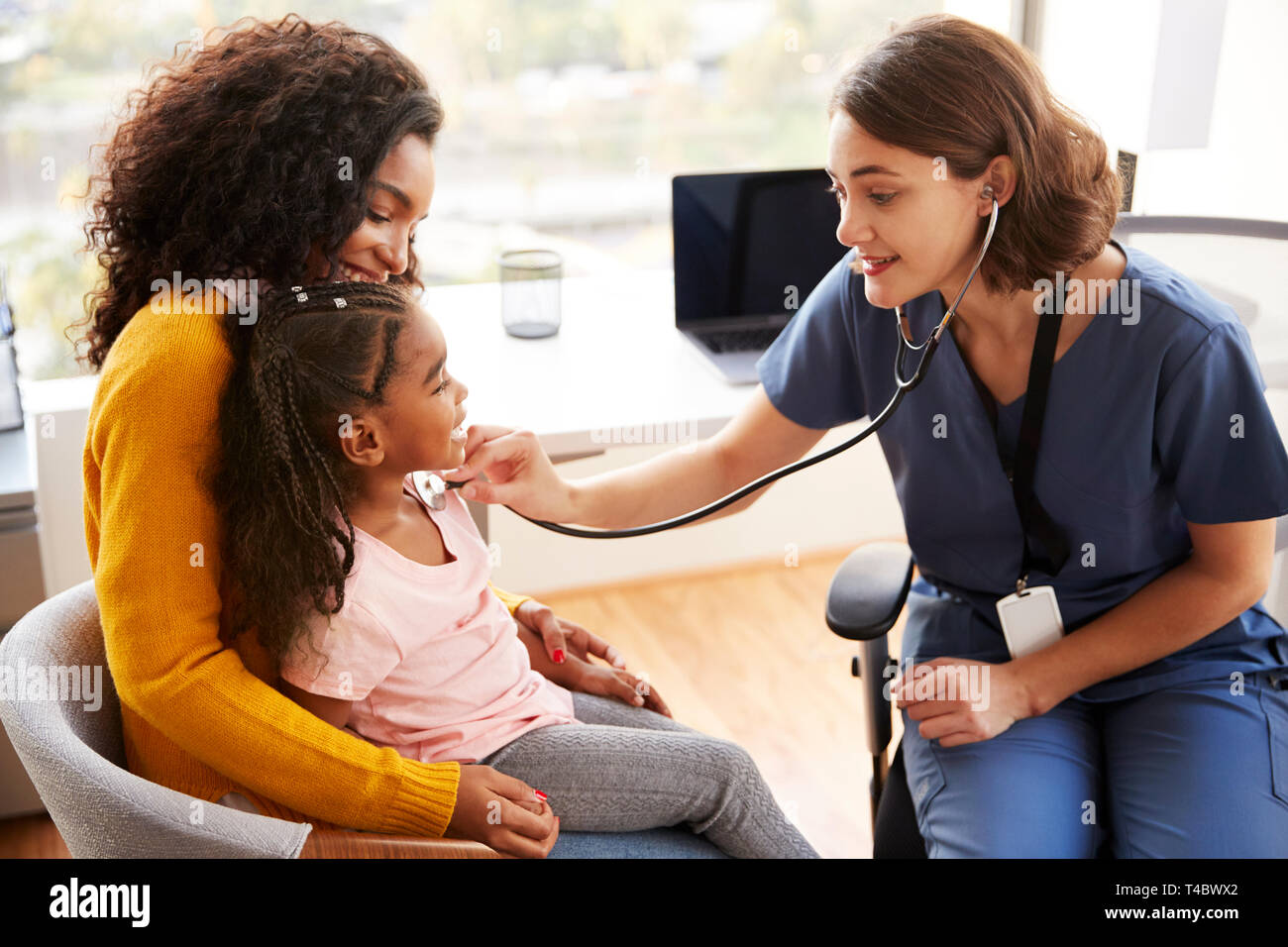 Female Pediatrician Wearing Scrubs Listening To Girls Chest With Stethoscope In Hospital Office Stock Photo