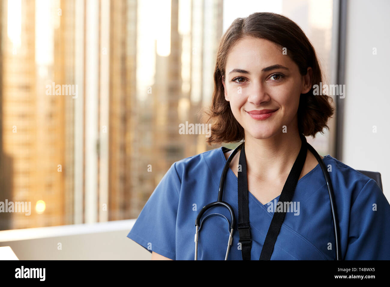 Portrait Of Smiling Female Doctor Wearing Scrubs With Stethoscope In Hospital Office Stock Photo