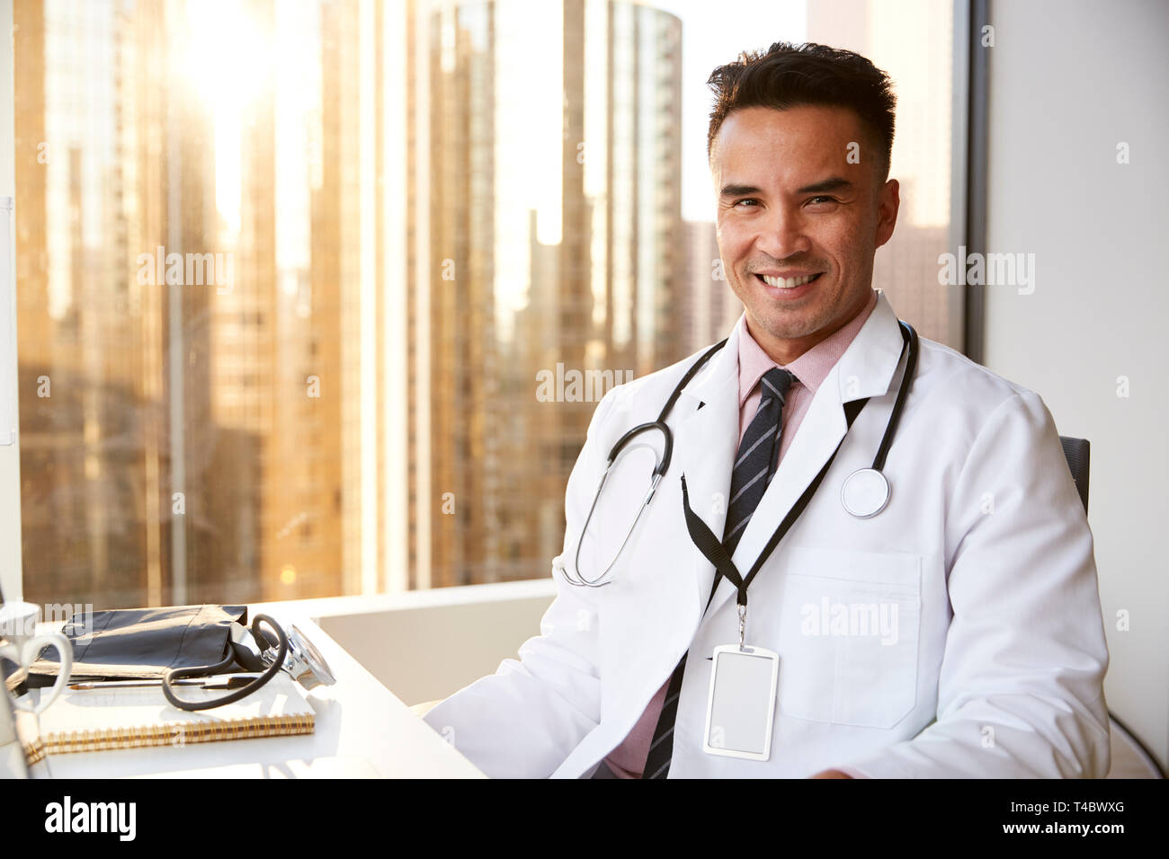 Portrait Of Smiling Male Doctor Wearing White Coat With Stethoscope In Hospital Office Stock Photo