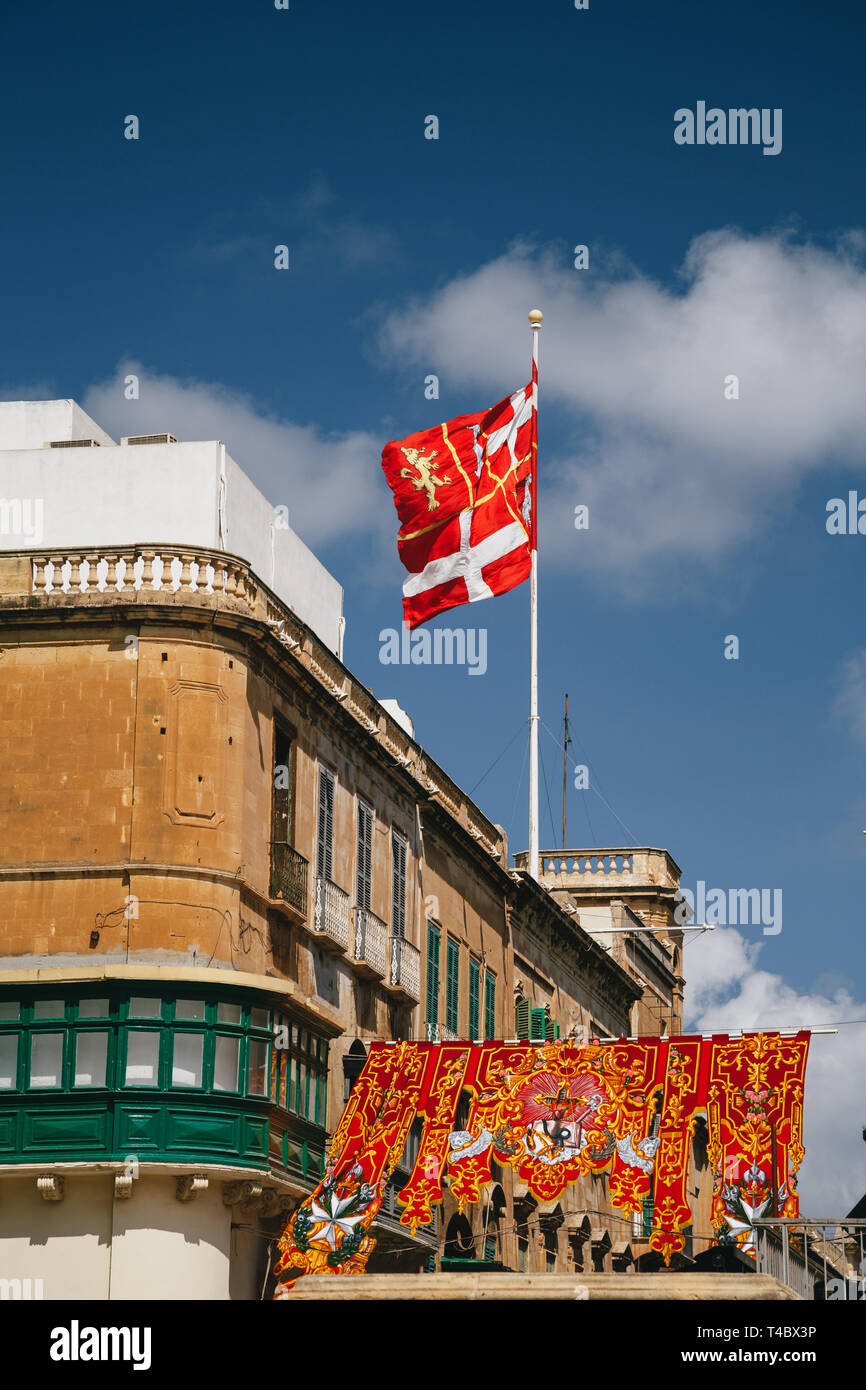 Maltese flag against a blue sky at the festively decorated street in the old town of Valletta, capital of Malta. Popular touristic destination and Stock Photo