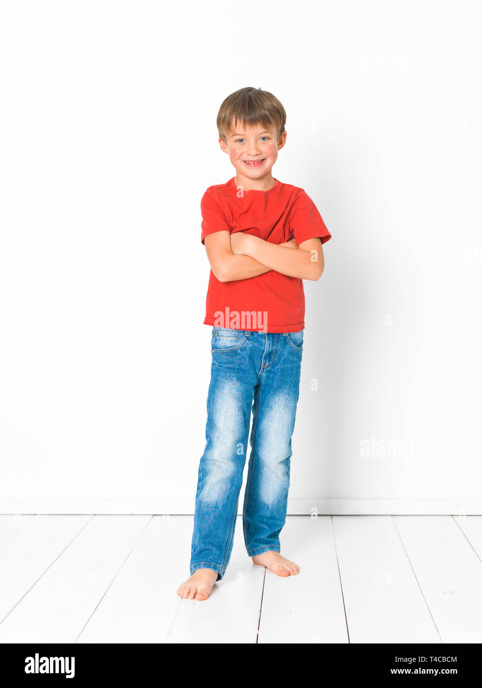 Usikker stykke er nok cute and blond boy with red shirt and blue jeans is posing on white wooden  floor in front of white background Stock Photo - Alamy