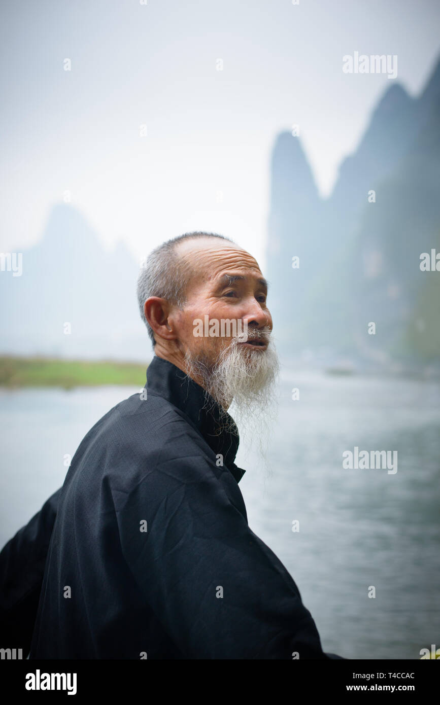 Portrait of a River Lee Cormorant Fisherman at dawn with karst peaks in the background. Guangxi Region of China. Stock Photo