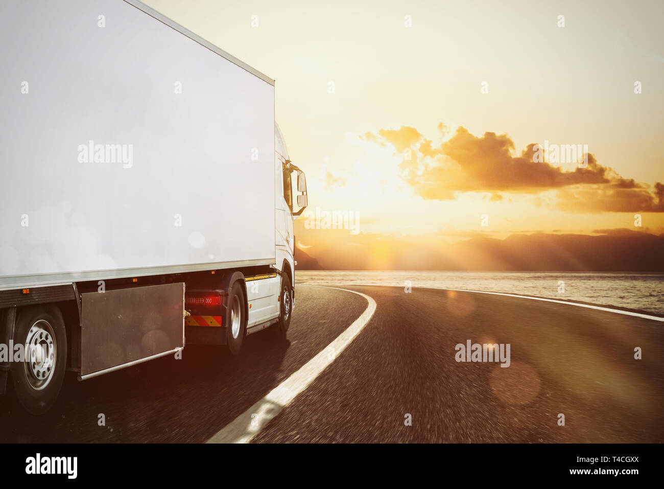 White truck moving on the road in a natural landscape at sunset Stock Photo