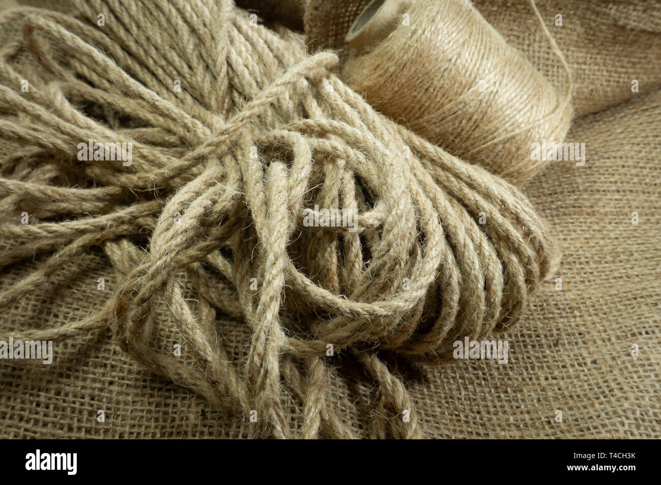Two spools of burlap threads or jute twine and coil of linen rope on sackcloth fabric in close-up on grey background Stock Photo