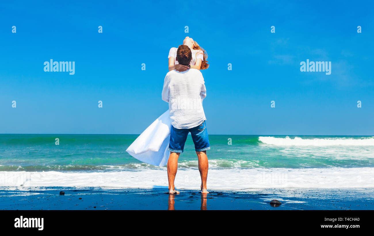 Happy family on honeymoon holiday - just married young man and woman have fun on black sand beach. Active lifestyle, people outdoor activity on summer Stock Photo