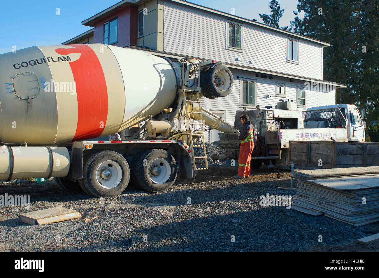 Cement truck with worker pouring cement outside new residential construction. Stock Photo
