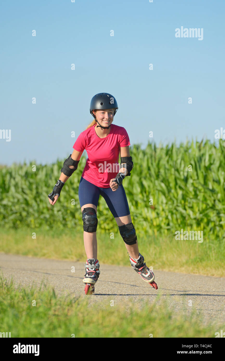 Teen rollerblading in summer on a small road, wearing a helmet and