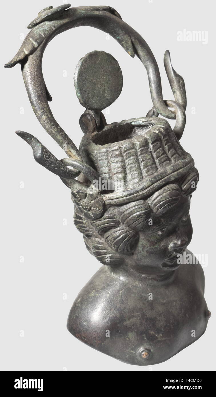 A Roman balsamarium, 1st/2nd century AD. Bronze with greenish patina. Container in the form of a bust of a cupid wearing a straw hat. Finely modelled facial features, silver inlaid eyes and nipples. The top of the hat with hinged lid. Side loops with ornamental rosettes. The movable handle terminating in bird's heads. The right loop slightly damaged, small hole at the back of the head. Height without lid 10 cm, with lid 14.5 cm. Provenance: Viennese private collection, 1980s, historic, historical, 20th century, ancient world, ancient world, ancie, Additional-Rights-Clearance-Info-Not-Available Stock Photo