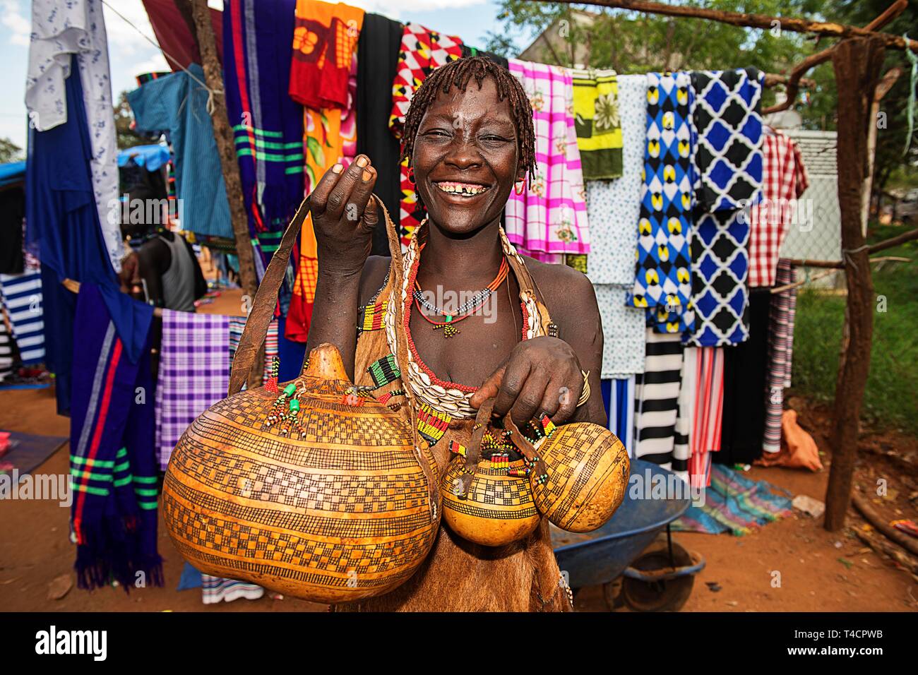 Laughing woman of the Hamer ethnic group sells artfully decorated calabashe pumpkins, market in Dimeka, Lower Omo Valley, Omo region, South Ethiopia Stock Photo