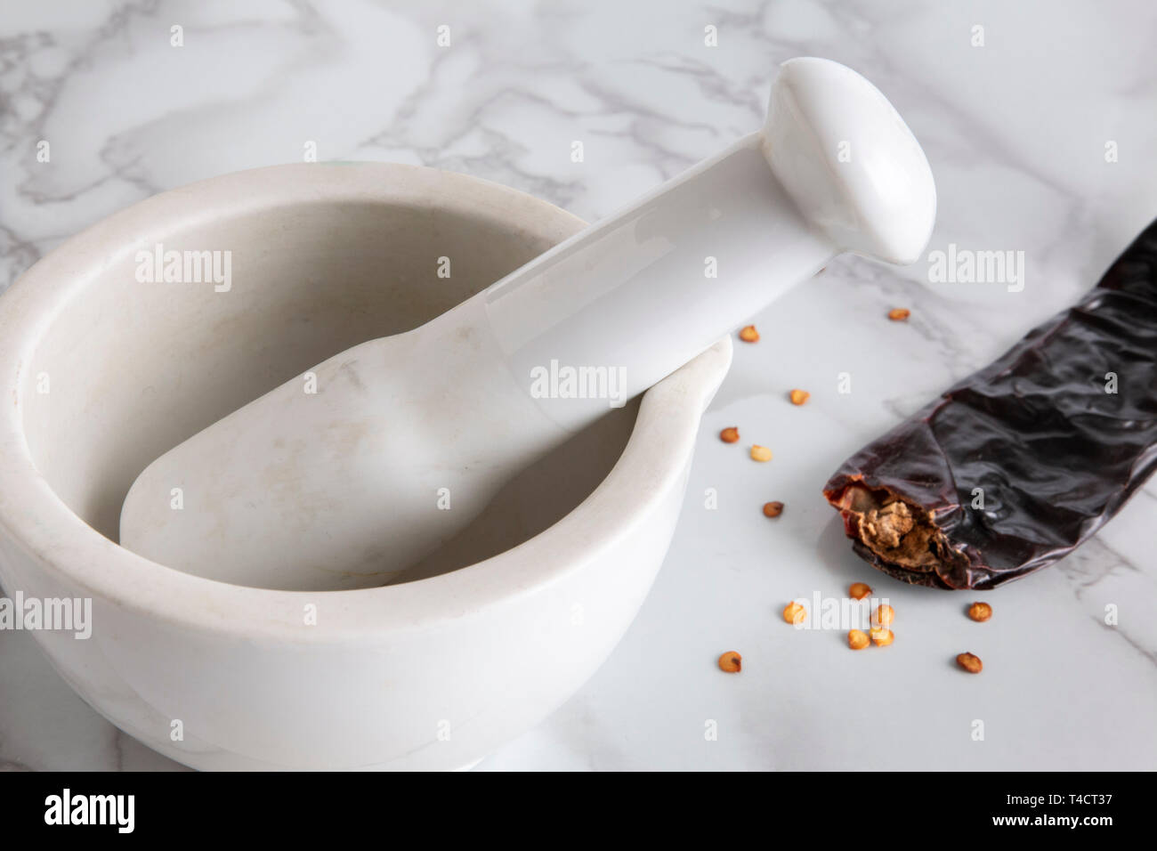 Close up of a pestle and mortar next to a dried chilli and chilli seeds Stock Photo