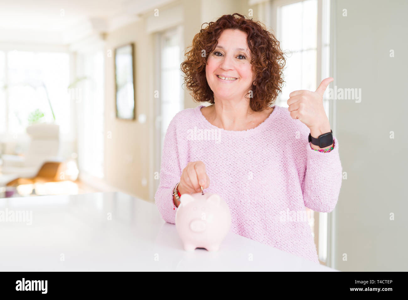 Senior woman saving money putting a coin inside piggy bank pointing and ...
