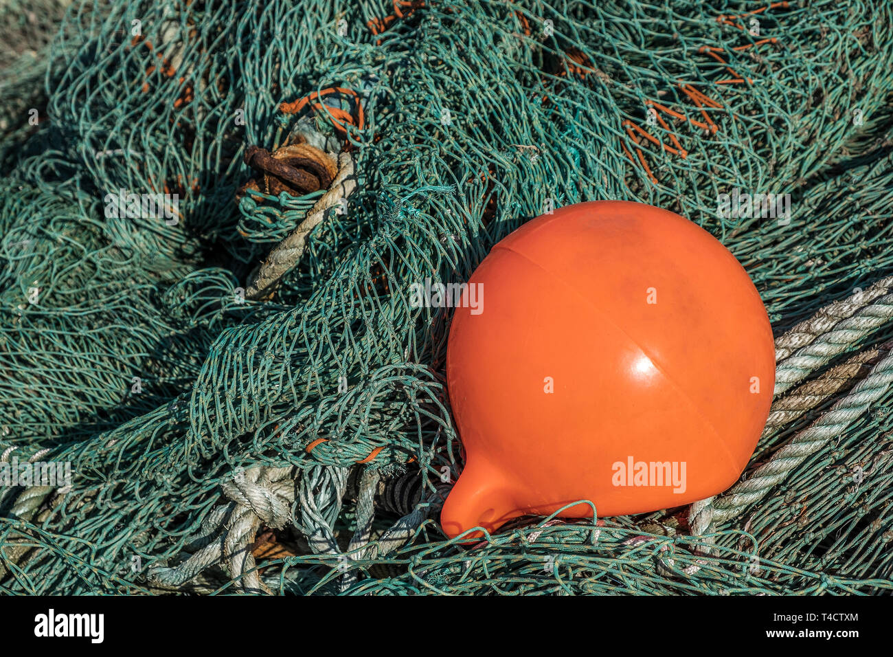 A tangled fishing net with a orange fishing buoy on top. Stock Photo