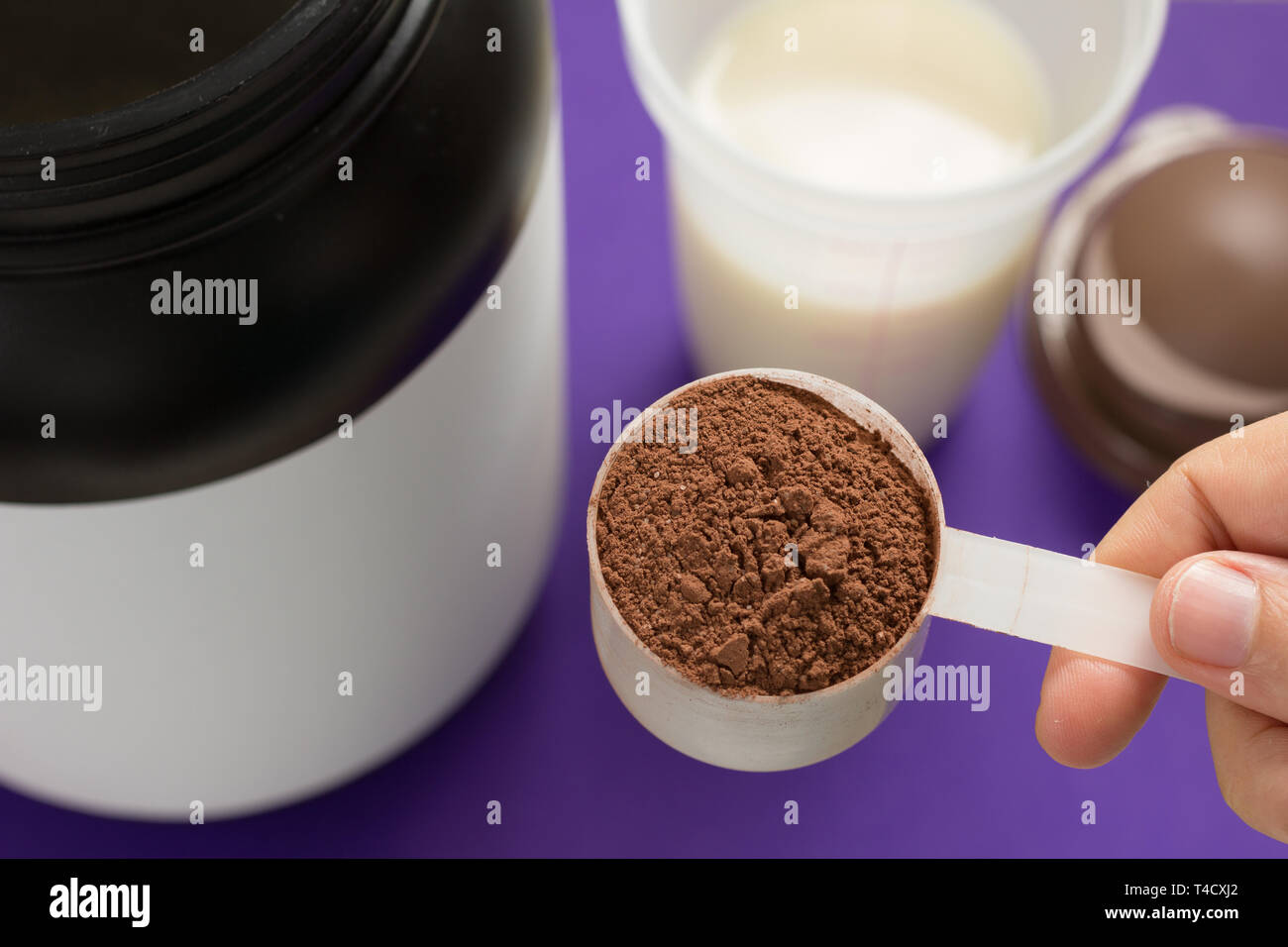 Whey protein food supplement for training and exercise. Perspective of person preparing protein shake. Chocolate flavour. Color background: violet. Stock Photo