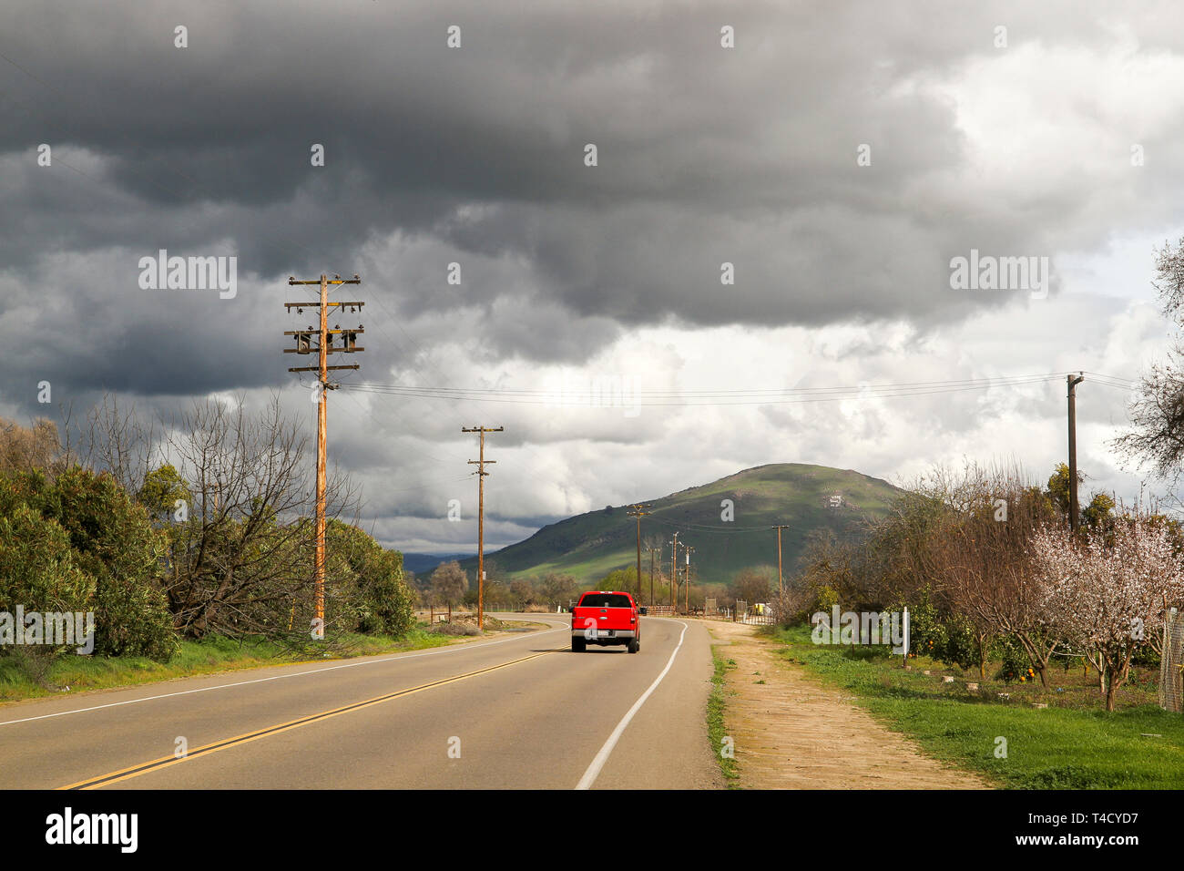 Red truck driving through farmland under stormy skies in Fresno County, California, United States Stock Photo