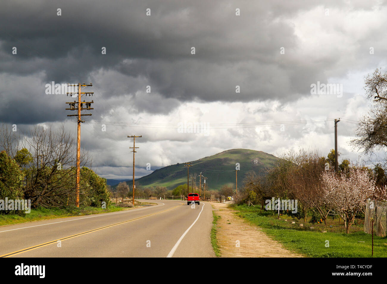 Red truck driving through farmland under stormy skies in Fresno County, California, United States Stock Photo