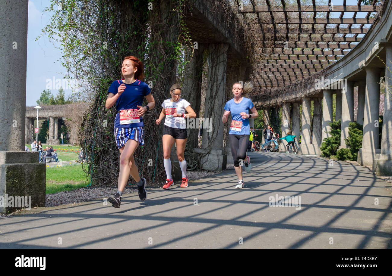 Three women in t-shirts with numbers run marathon in the park in spring. Wroclaw, Poland - April 7, 2019 Stock Photo