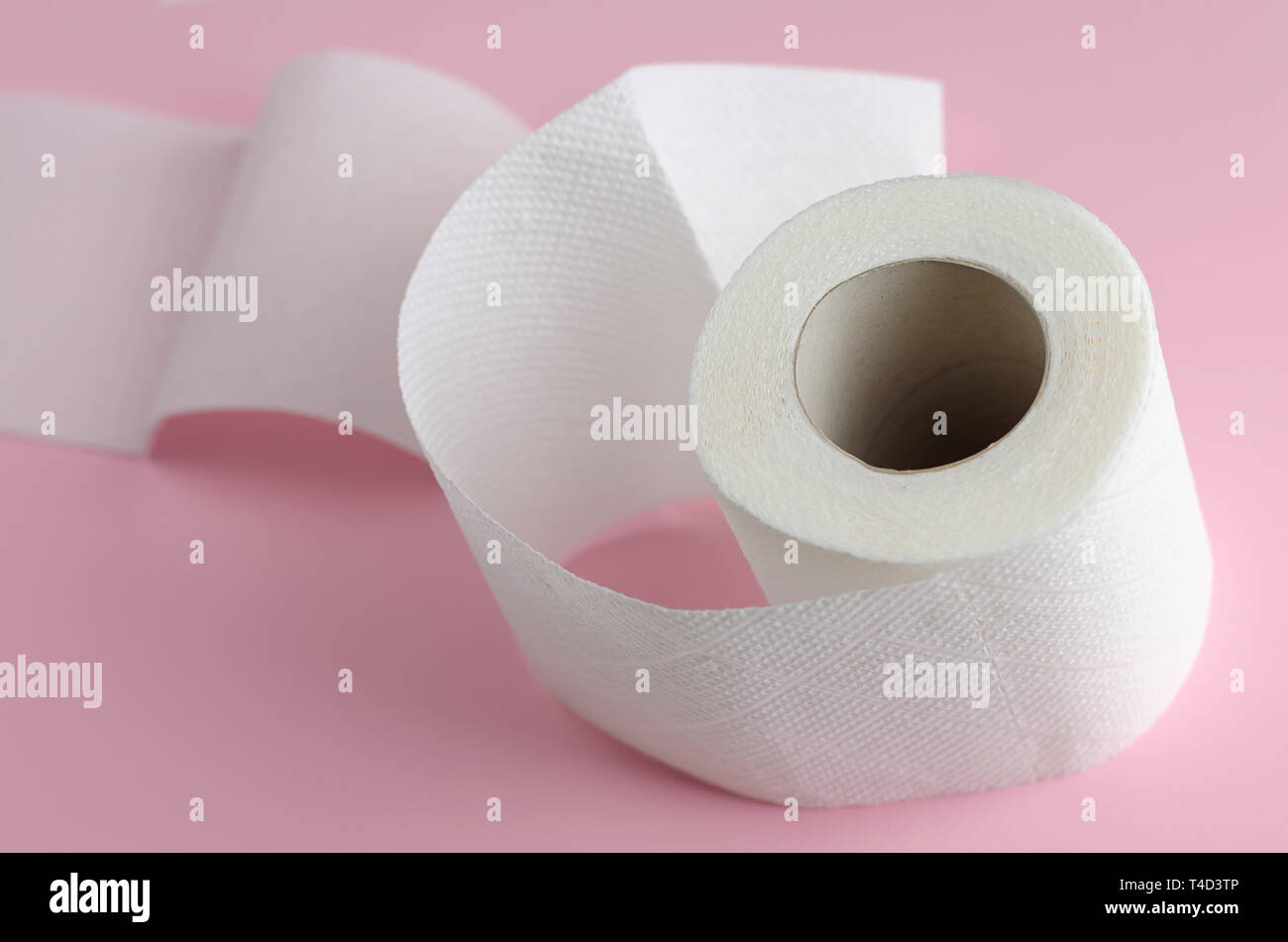 Single white toilet paper roll on pastel pink background. Space for