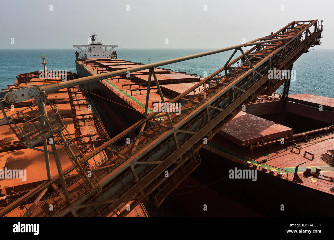 Port operations for managing and transporting iron ore. Unloading fines ore from TGV transhipper boat into hold of OGV ocean going vessel at sea Stock Photo