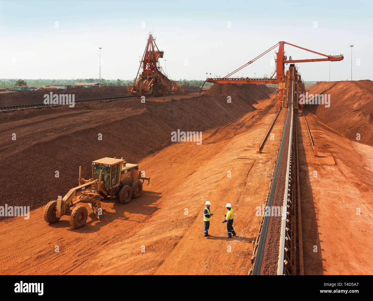 Port operations for managing & transporting iron ore. Along conveyor belt to newly built stacker with stacker reclaimer to left plus grader vehicle. Stock Photo