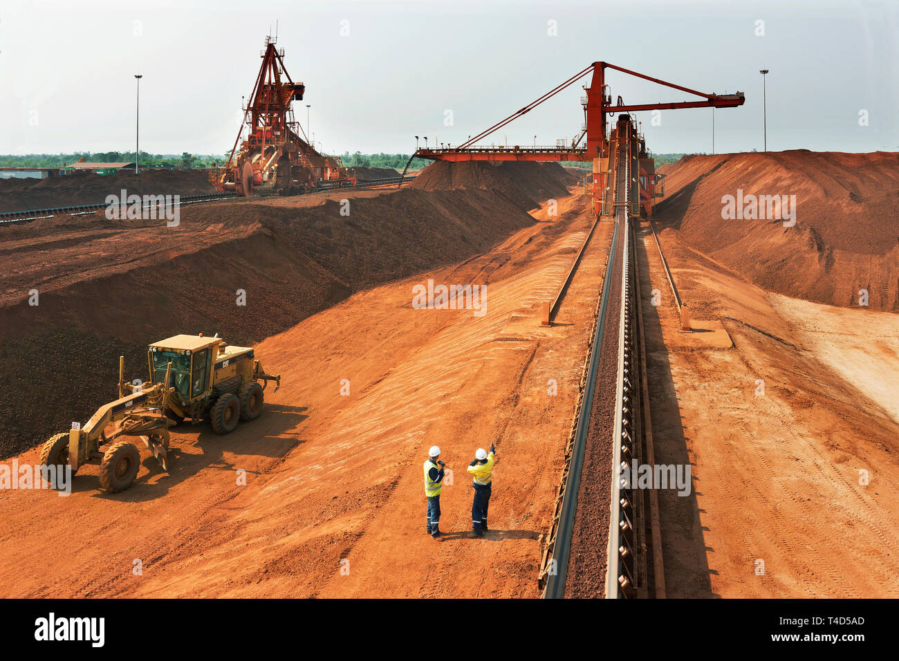 Port operations for managing & transporting iron ore. Along conveyor belt to newly built stacker with stacker reclaimer to left plus grader vehicle. Stock Photo