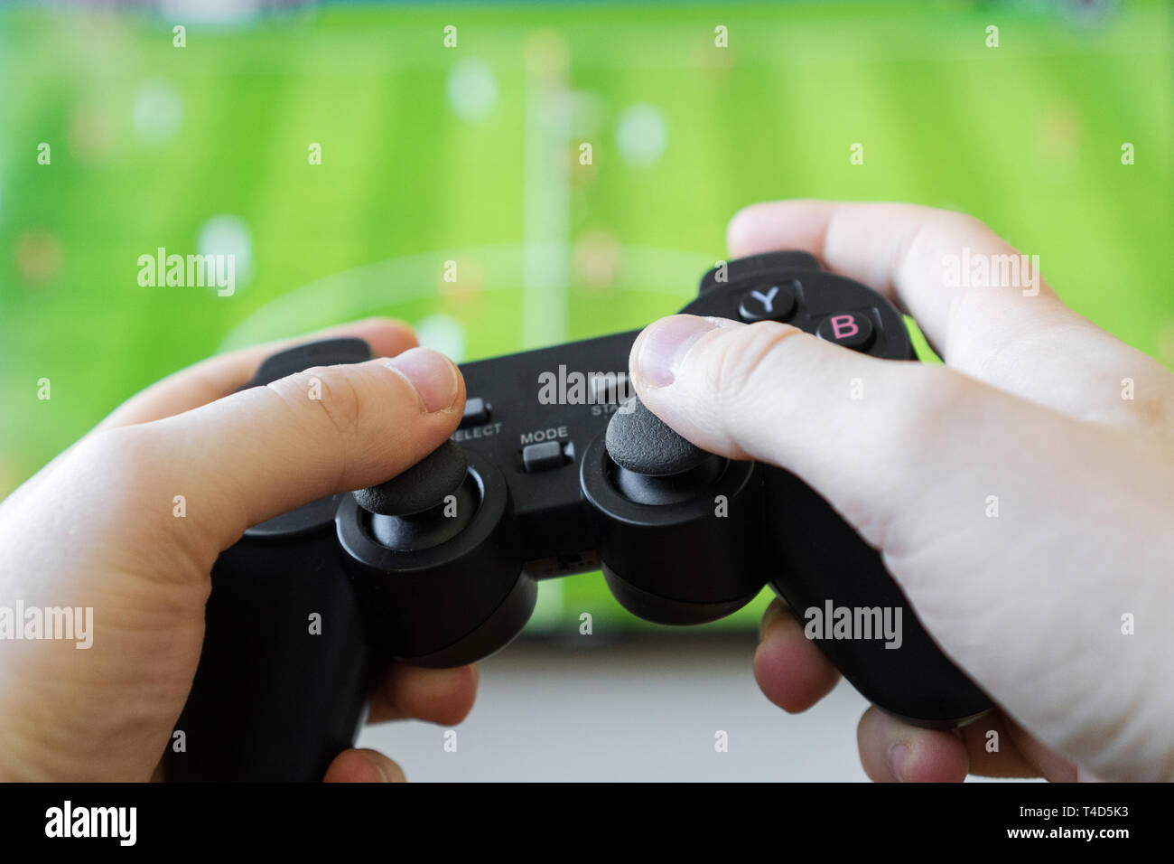 Man playing soccer video game on TV. Gamepad controller in hands Stock