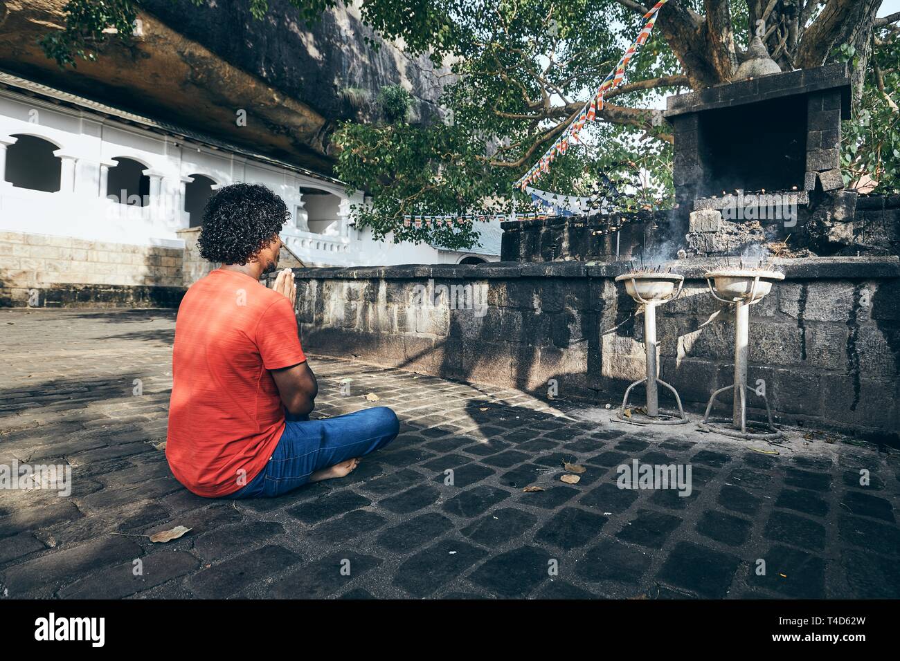 Young man (Buddhist) praying against ancient cave temple complex. Dambulla, Sri Lanka. Stock Photo
