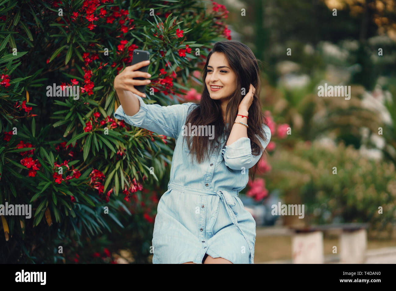 A beautiful young girl in a blue dress sitting near the flower tree ...