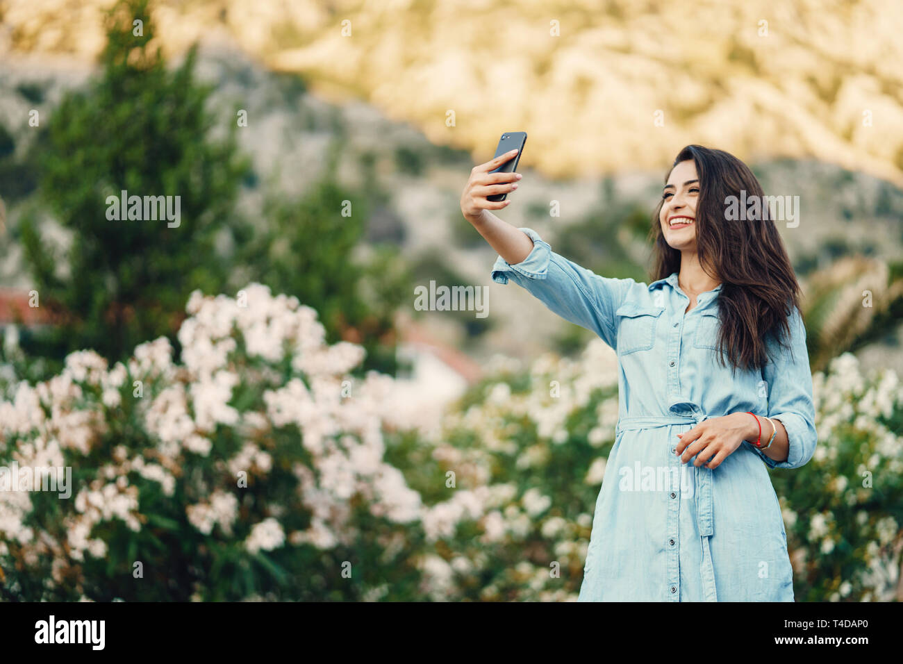 A beautiful young girl in a blue dress standing near the flower tree ...