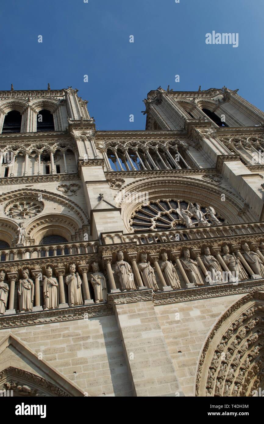 Looking up at Notre-Dame's famous bell towers against a bright blue sky. Ancient medieval cathedral in Paris, France. Tall, ornate stone towers. Stock Photo