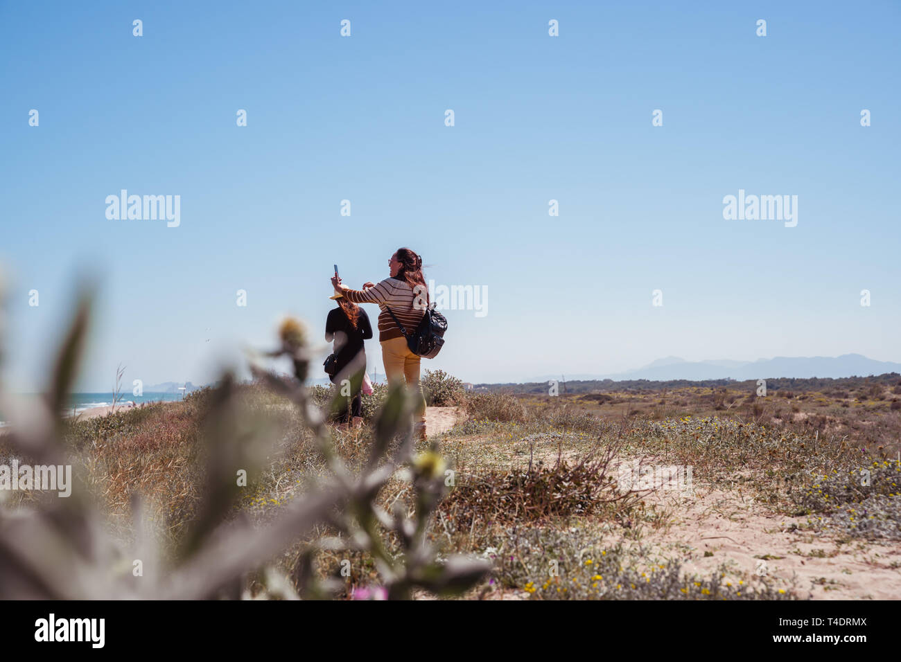 Valencia,Spain - April 13, 2019: Mid age woman taking selfie near the beach. Bushes and dry ground. Stock Photo