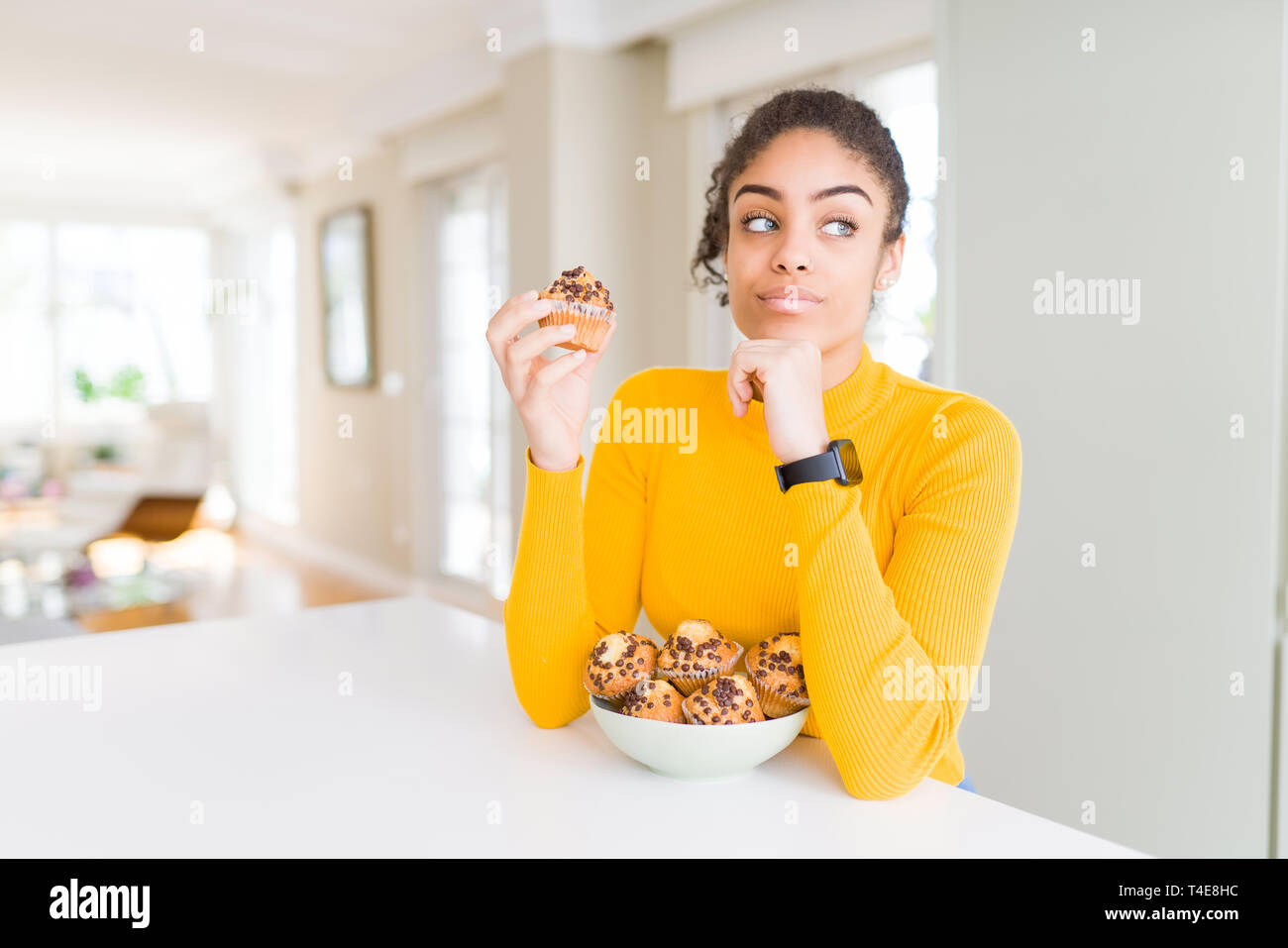Young african american woman eating chocolate chips muffins serious face thinking about question, very confused idea Stock Photo