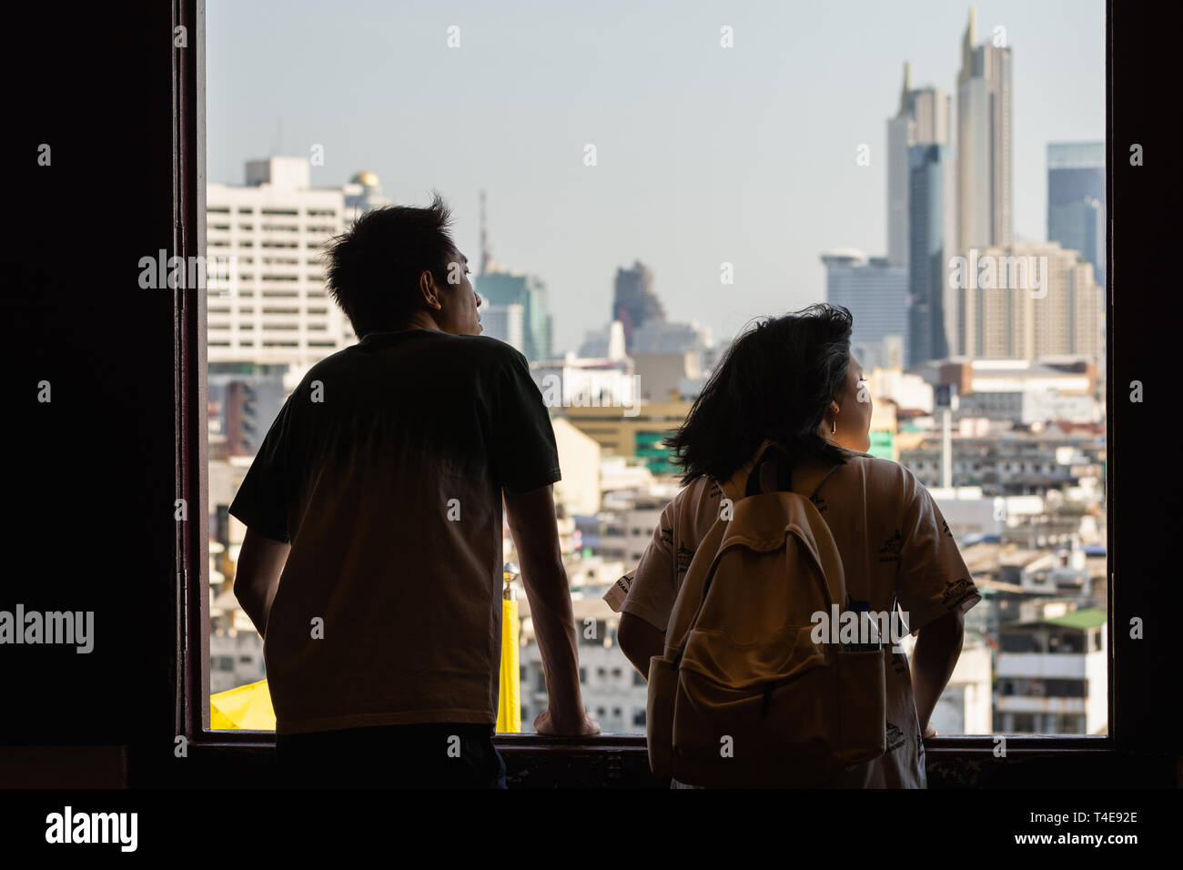 BANGKOK, THAILAND - MARCH 2019: Asian couple looking out of Golden Mount Wat Saket temple window overlooking Bangkok city skyline. Stock Photo