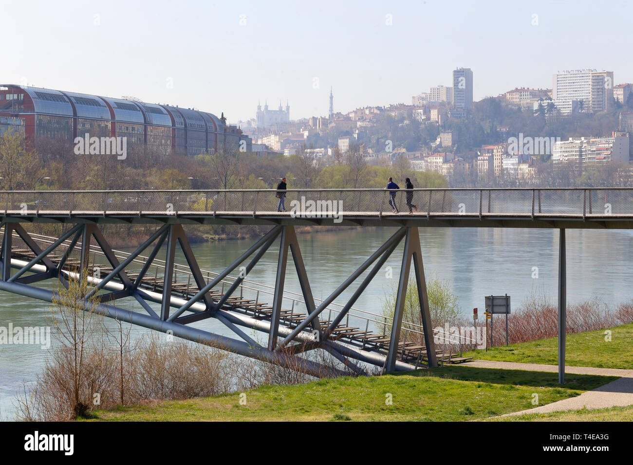 People on the Passerelle de la Paix pedestrian and bicycle bridge over the Rhone River with houses of Boucle-Gros Caillou, Lyon in the background Stock Photo